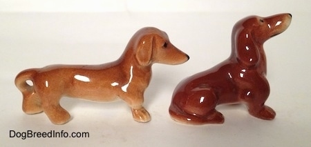 The right side of two different Dachshund figurines. One figurine is sitting and the other is standing.