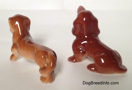 The back left side of a two Dachshund figurines that are different. The figurines tails are attached to there legs.