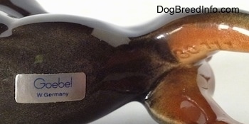 Close up - The underside of a Doberman Pinscher figurine. On the underside there the sticker of Goebel W.Germany and across its back right leg is the numbers - 30777.