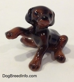 The front left side of a miniature black and brown Doberman Pinscher puppy with its paw up figurine. The figurine has black circles for eyes.