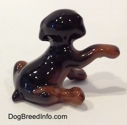 The right side of a miniature black and brown Doberman Pinscher puppy with its paw up figurine. The figurine has a short body.