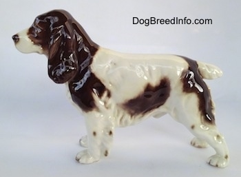 The left side of a white with brown English Springer Spaniel figurine. The figurine has a short white tail and it has a brown to white to brown muzzle.