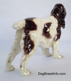 The back right side of a figurine of a white with brown English Springer Spaniel. The tail of the figurine is short, it is up and level with its body.