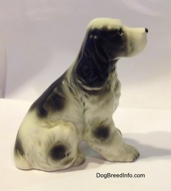 The right side of a figurine of a black and white English Springer Spaniel figurine in a sitting pose. The ears of the figurines are hard to differentiate from its head.