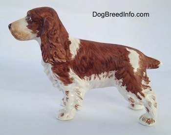 The left side of a brown and white English Springer Spaniel figurine. The figurine has long legs and small paws. The legs have hair on the back of them.
