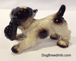 The left side of a figurine of a liver and white English Springer Spaniel puppy in a play bow pose. The figurine has white paws with brown tips.