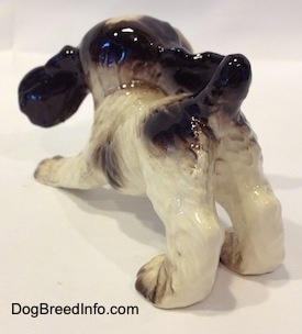 The back left side of an English Springer Spaniel puppy figurine that is in a play bow pose. The figurine has brown spots along its body.