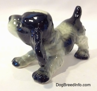 The front left side of a black and white English Springer Spaniel puppy figurine in a play bow pose. The figurine has black paws.