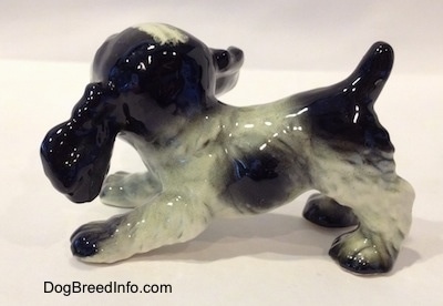 The left side of a figurine of a black and white English Springer Spaniel puppy in a play bow pose figurine. The figurine has a short arched up black tail.