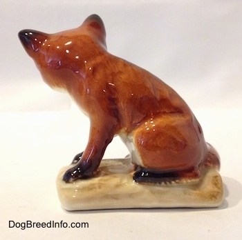 The left side of a red fox porcelain figurine that is sitting on a log. The figurine is glossy.
