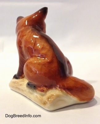 The back left side of a red fox porcelain figurine. The figurine has a black streak going down its back.