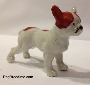 The front right side of a white with red bone china French Bulldog figurine. The figurine has black dots around its muzzle.