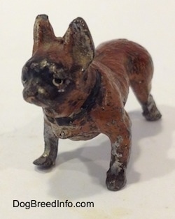 The front left side of a brown with black French Bulldog figurine that has chips and scratches all over it.