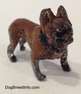 The front right side of a metal figurine of a brown with black French Bulldog. The figurine has a black collar on.