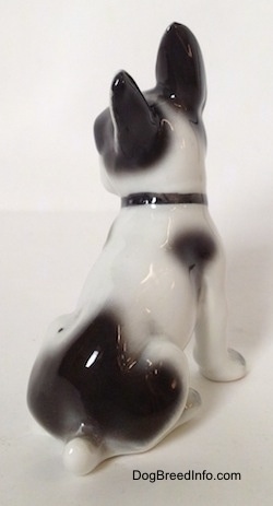 The back right side of a figurine of a white and black French Bulldog in a sitting pose. The figurine has a short white tail in the midst of a large black spot.