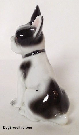 The back left side of a white and black French Bulldog figurine in a sitting pose. The figurine is wearing a black collar.