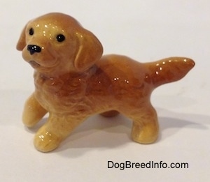 The left side of a Golden Retriever puppy figurine. The figurine has black circles for eyes and its ears are drapped along the side of its head.