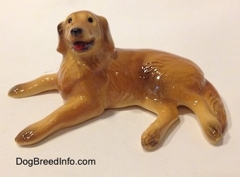The left side of a Golden Retriever figurine in a laying down pose. The figurine has black circles for eyes, its mouth is open and tongue is sticking out.