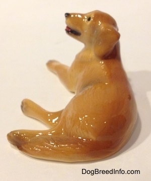 The back of a figurine of a Golden Retriever in a laying down pose. The figurine has a long tail.