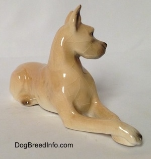 The front right side of a tan Great Dane figurine that is laying down. The figurine is glossy.