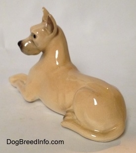 The back left side of a figurine of a tan Great Dane that is laying down. The figurine has a long tail next to its leg.