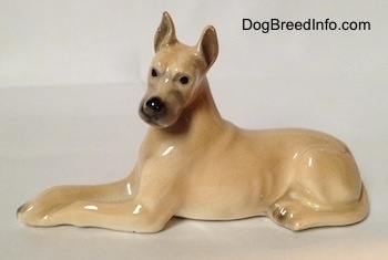 The left side of a tan Great Dane figurine that is laying down. The figurine has black circles for eyes.