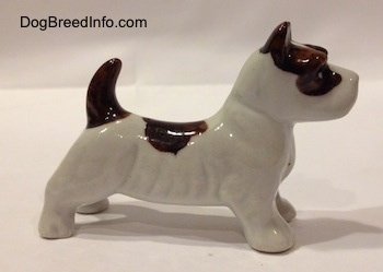 The right side of a figurine of a white with brown bone china Jack Russell Terrier dog figurine. The figurine has its tail arched into the air.