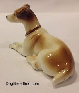 The back left side of a laying down brown and white Jack Russell Terrier figurine. The figurine has a short tail and it is glossy.