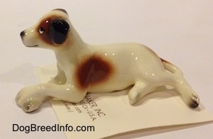The left side of a Jack Russell Terrier dog in a lying down pose figurine. The figurine has flopped over black ears.