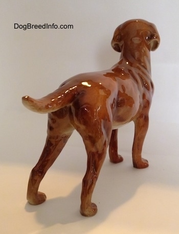 The back right side of a figurine of a brown Labrador Retriever. The tail of the figurine is up and level with its body.