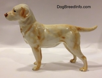 The left side of a yellow Labrador Retriever. The retriever has black circles for eyes. The figurine has small paws and longlegs.