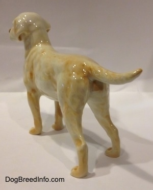 The back left side of a figurine of a yellow Labrador Retriever. The figurine has ears that are attached to its head.