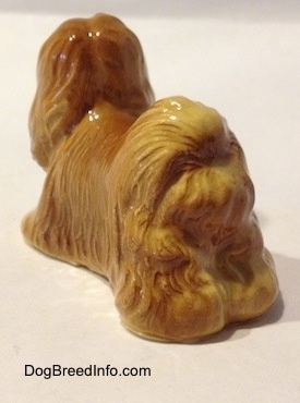 The back left side of a brown Lhasa Apso figurine. The figurine has a hairy tail on its back.