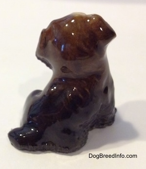 The back of a ceramic black, brown and tan puppy figurine. The figurine is very glossy.