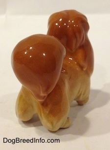 The back right side of a figurine of a brown with tan Pekingese puppy figurine. The tail of the figurine is arched onto its back.