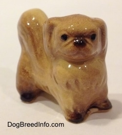 The front right side of a tan with brown Pekingese figurine. The figurine has black circles for eyes.