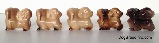 The left side of a line-up of different color variations of a Pekingese figurine. The figurines have black paws.