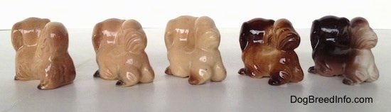 The back left side of a line-up of different color variations of a Pekingese figurine. It is hard to differentiate the ears of the figurines from there heads.