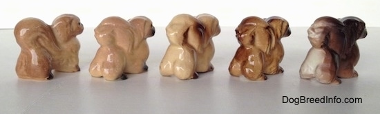 The back right side of a line-up of different color variations of a Pekingese figurine.