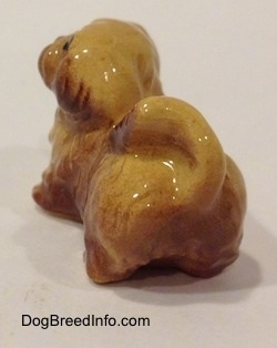 The back left side of a figurine of a brown and tan Pekingese puppy. The figurine is glossy.
