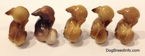 The back of five different color variations of a Pekingses puppy seated figurine. The figurines has there tails curled onto there backs.