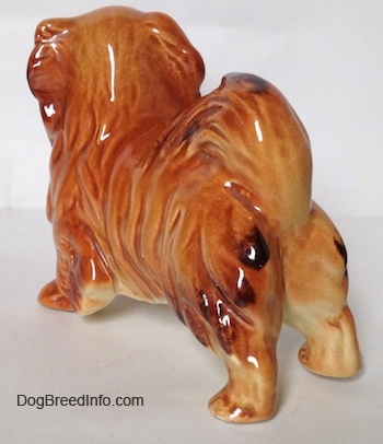 The back left side of a brown and tan with black Pekingese figurine. The figurine has short legs.