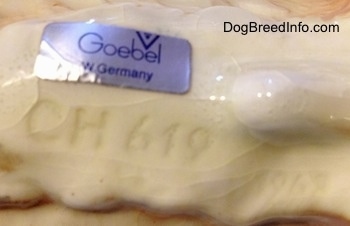 The underside of a Pembroke Welsh Corgi figurine. There is a sticker on the figurine, the sticker reads - Goebel W.Germany - and under the sticker is a series of letters/numbers - CH619.