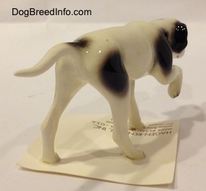 The back right side of a figurine of a white with black Pointer in a pointing pose. The figurine has a long tail that is level with its body.