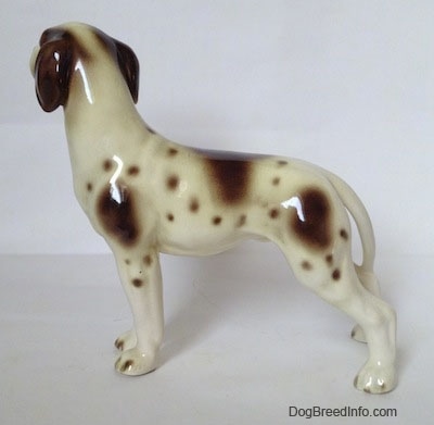 The left side of a white and tan Pointer with brown patches figurine. The figurine has a long tail.