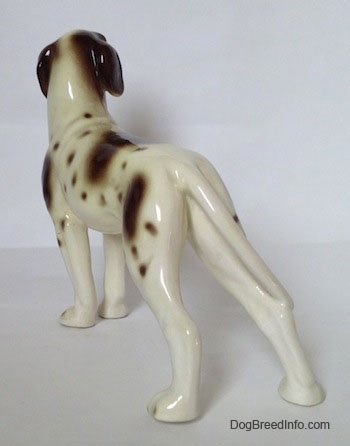 The back left side of a white and tan figurine of a Pointer with brown patches. The figurine has long legs.