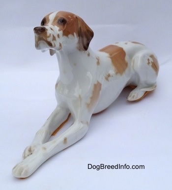The front left side of a white with brown porcelain Pointer figurine in a lying down pose. The figurine is looking up and to the left.