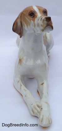 A porcelain white with brown figurine of a Pointer in a lying pose. The figurine has a very detailed face.