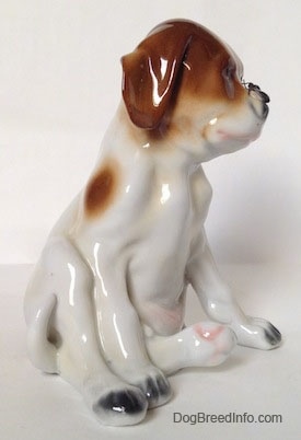The right side of a figurine of a Pointer puppy sitting with a fly on its nose. The figurine has black tipped paws.