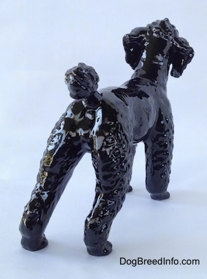 The back right side of a figurine of a black Poodle. The figurine has medium length legs.